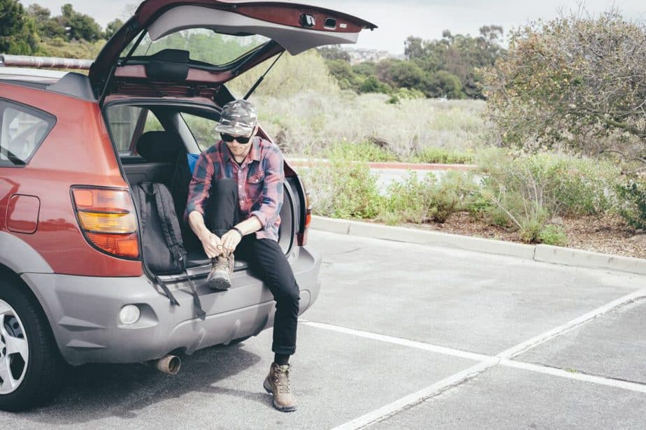 Male hiker sitting on car boot tying hiking boot laces, Crystal Cove State Park, Laguna Beach,